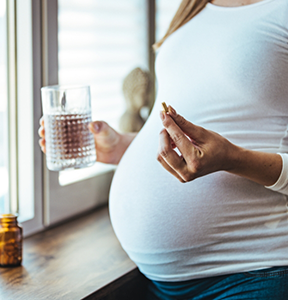 Pregnant person taking a pill with water