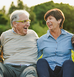 Senior couple laughing together with green trees in the background