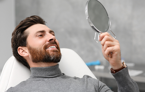 Man in the dental chair looking at his smile in a mirror