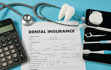 Dental insurance paperwork next to a tablet, a calculator, a stethoscope, and dental tools